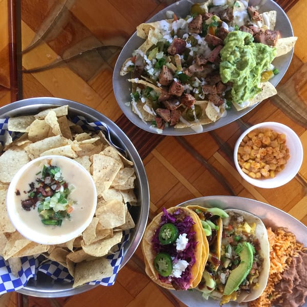 Overhead view of a Mexican feast with nachos, tacos, rice, beans, corn, chips, and queso.