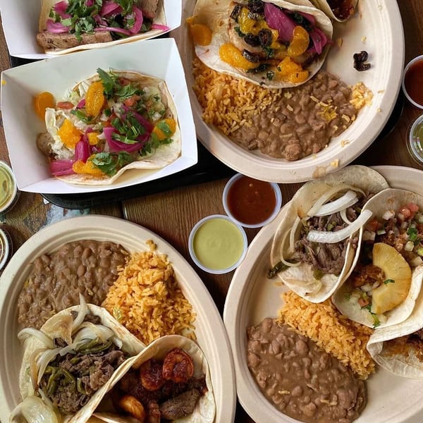 An overhead view of several plates and containers filled with various tacos, rice, and beans.